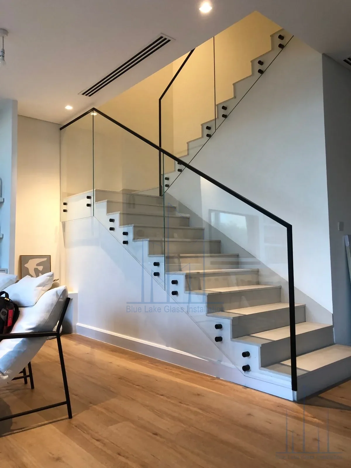 Clear glass railing on a residential staircase with black handrail