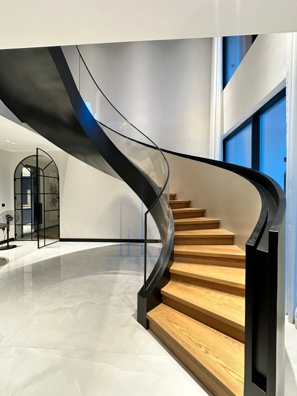 Curved staircase with clear glass railing and black metal handrail